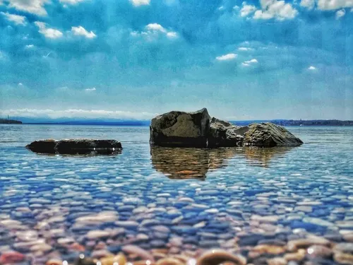 Steine liegen im klaren Wasser unter blauem Himmel.