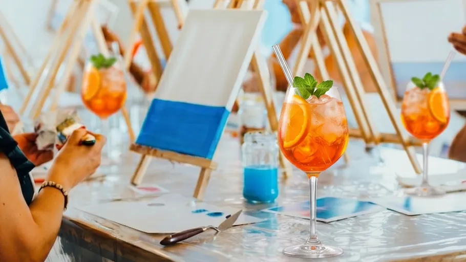 Künstler malen an Staffeleien mit Cocktails daneben.