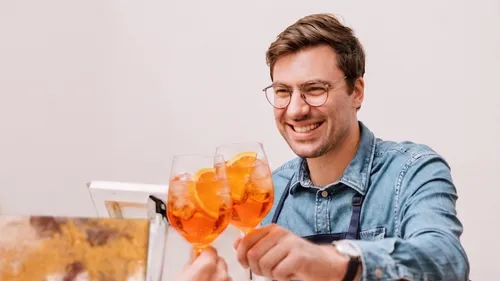 Smiling man toasting with orange drinks indoors.