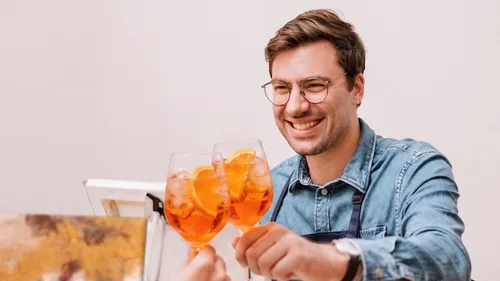 Man smiling, toasting with orange cocktails.
