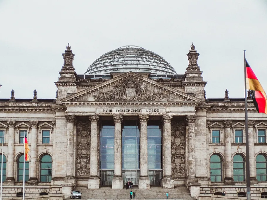 Reichstag-Gebäude, majestätisch, mit Flaggen, unter grauem Himmel.