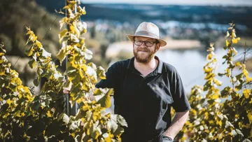 Man in vineyard wearing hat, scenic background.