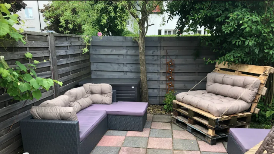 Cozy patio with pallet furniture, surrounded by fence.