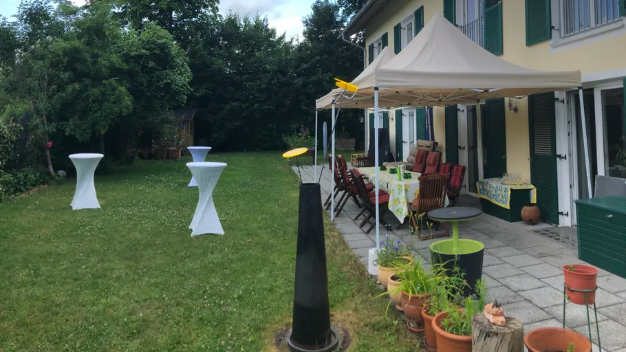 Garten mit Zelt und gedeckten Tischen neben Haus.