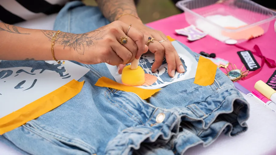 Person schabloniert Design auf Jeansstoff.