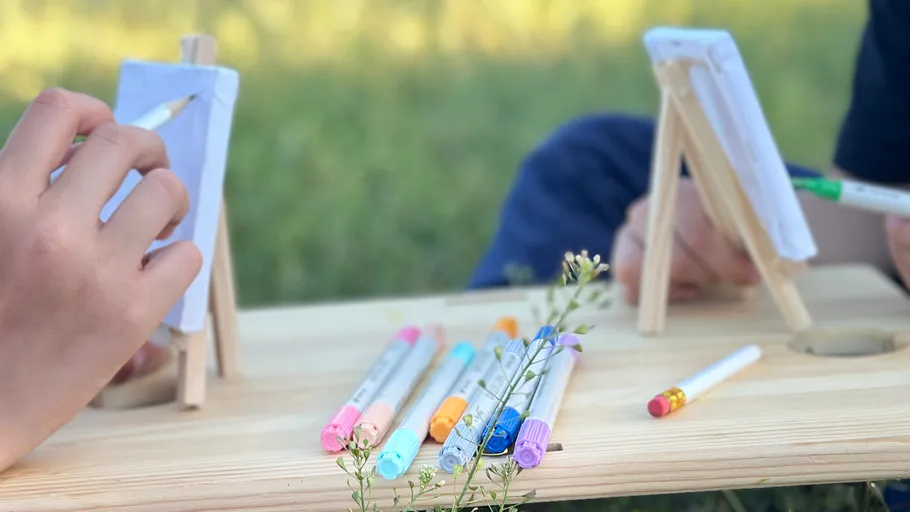 Hands drawing on small easels with markers outdoors.