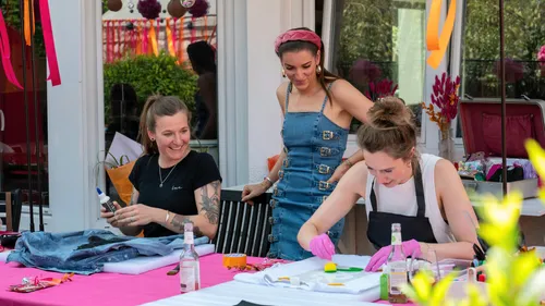 Women crafting at outdoor table, colorful decorations.