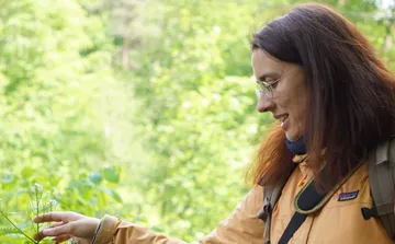 Frau zeigt auf Pflanze im Wald.