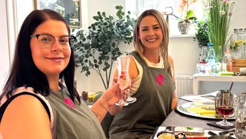 Zwei Frauen lächeln, sitzen an Esstisch.
