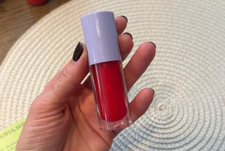 Hand holding red lip gloss over circular mat.