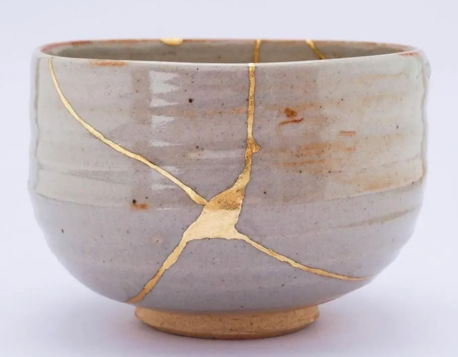 Ceramic bowl with gold repairs on white background.
