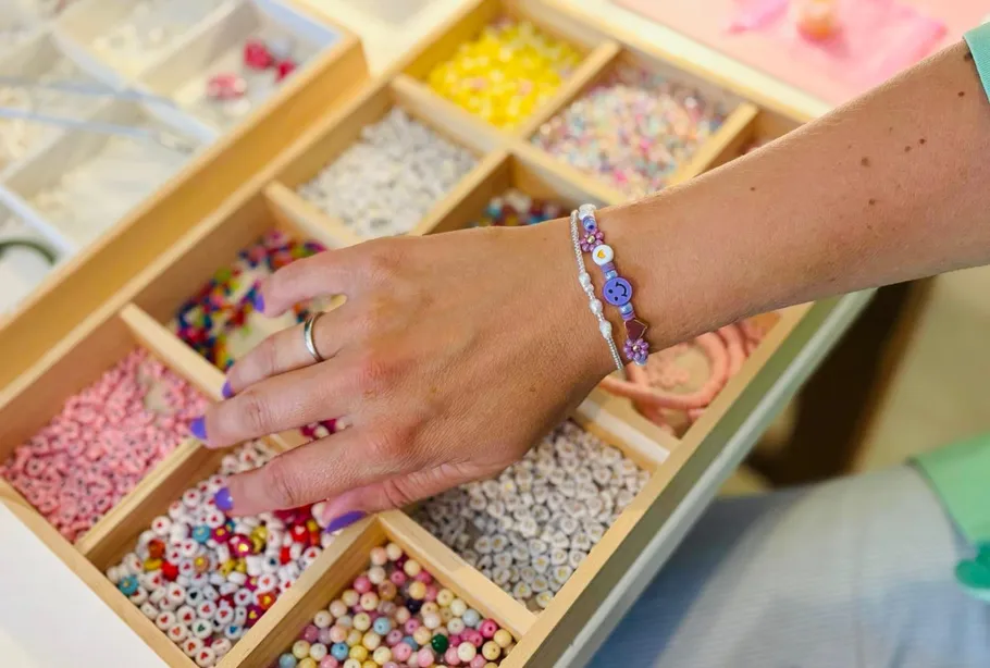 Hand selecting beads from organized wooden box.