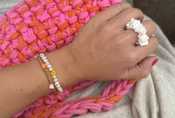 Hand mit Armbändern auf gestrickter pink-orangener Tasche.