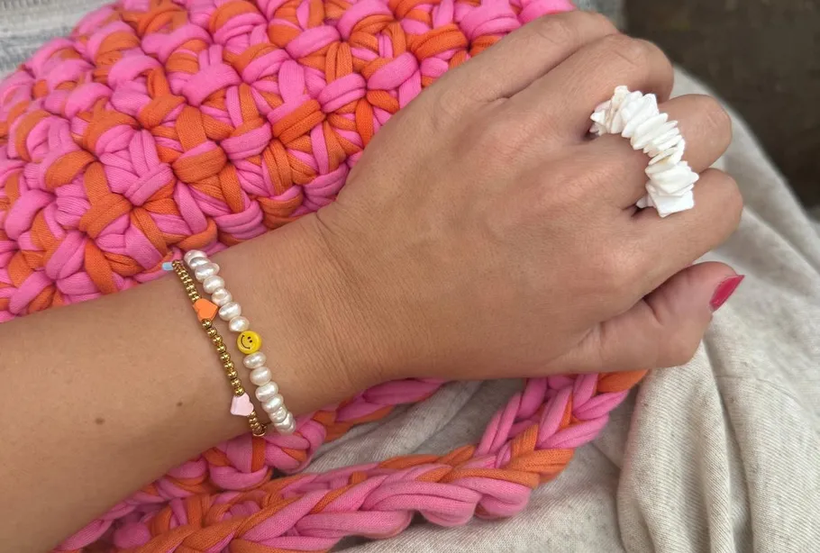 Hand wearing bracelets on knitted pink-orange bag.