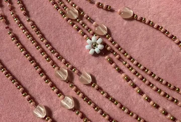 Perlenketten mit Blume auf rosa Hintergrund.