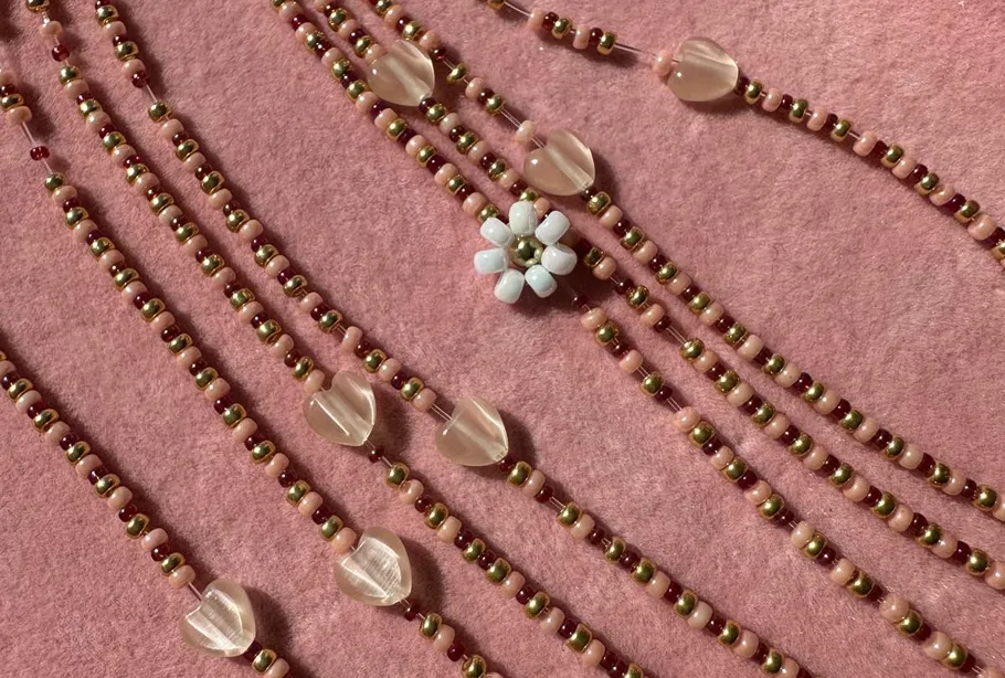 Beaded necklaces with flower on pink background.