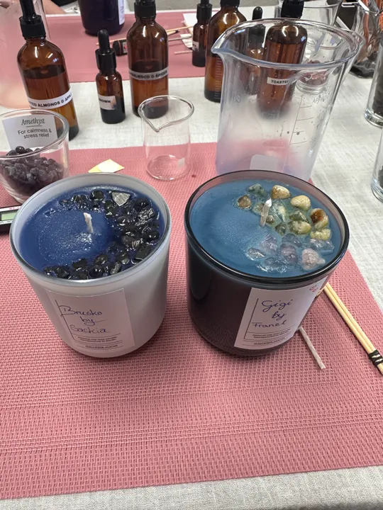 Kerzen mit Kristallen auf rosa Matte, umgeben von Flaschen.