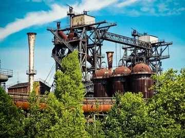 Outdoor industrial complex surrounded by trees, in sunny weather.