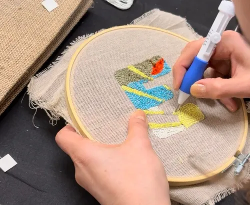 Person using punch needle for embroidery design.
