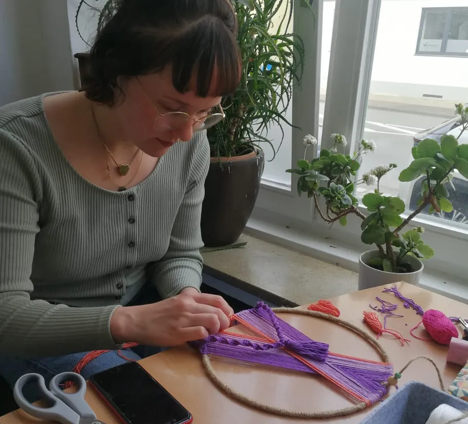 Person erstellt Garnkunst an einem Innentisch.