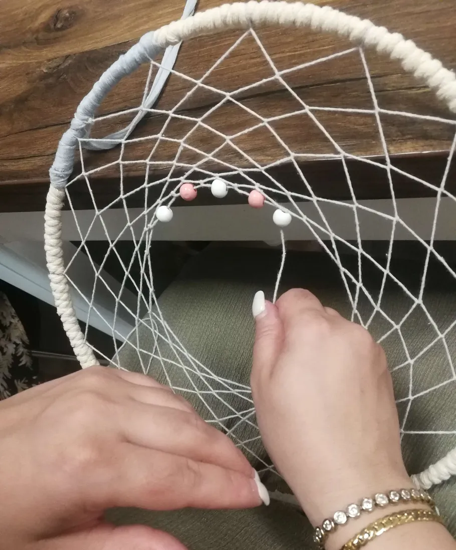 Hands weaving a dreamcatcher with beads.