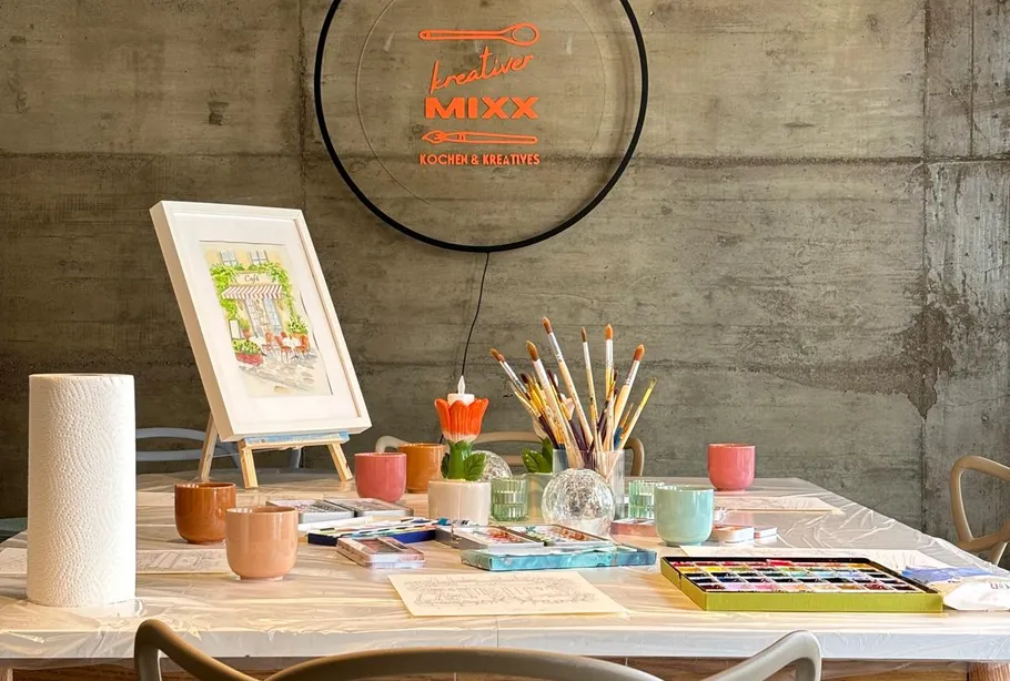 Art supplies on table, wall with neon sign.