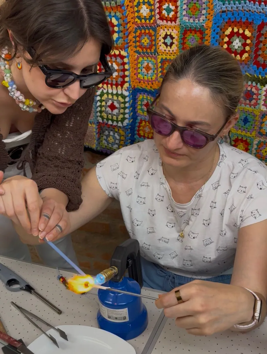 Two women making glass beads with a torch.