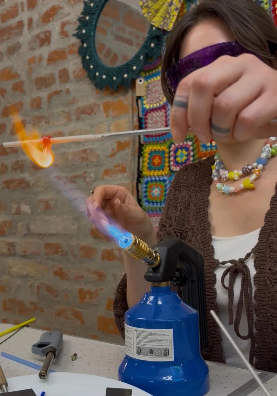 Person creating glass art using a flame torch.