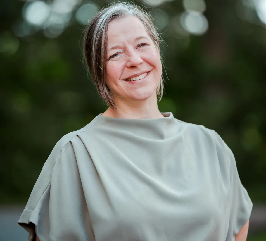 Smiling woman posing outdoors with blurred background.