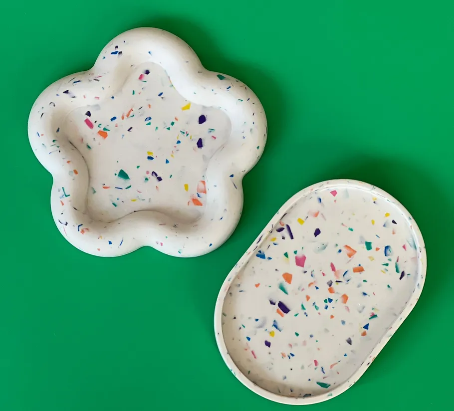 Zwei Terrazzo-Tabletts auf grünem Hintergrund.