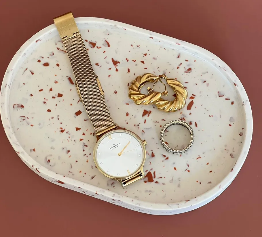Gold watch, ring, earrings on speckled tray.