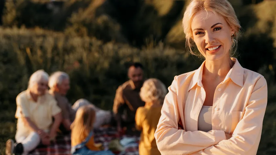 Woman smiling with family picnic in background.