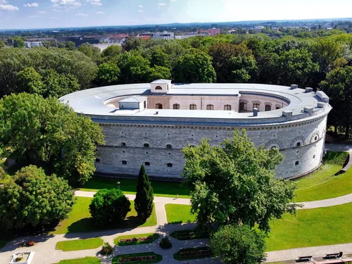 Historisches Gebäude umgeben von grünen Bäumen und Blumen.