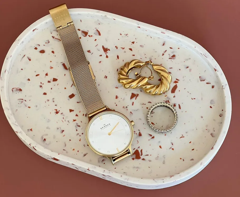 Goldene Uhr, Ohrringe, Ring auf gesprenkeltem Tablett.