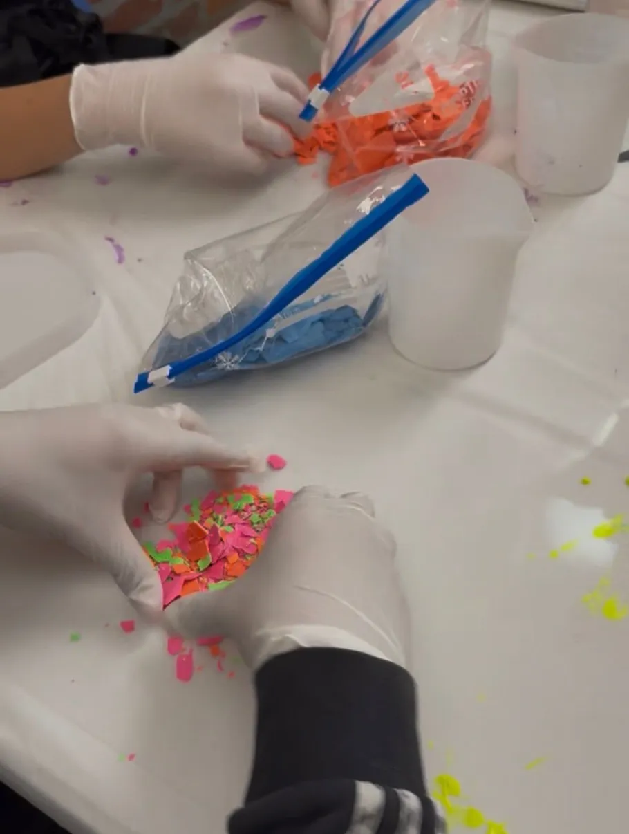 Gloved hands sorting colorful small pieces on table.