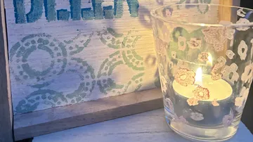Candle in floral holder beside decorated board.