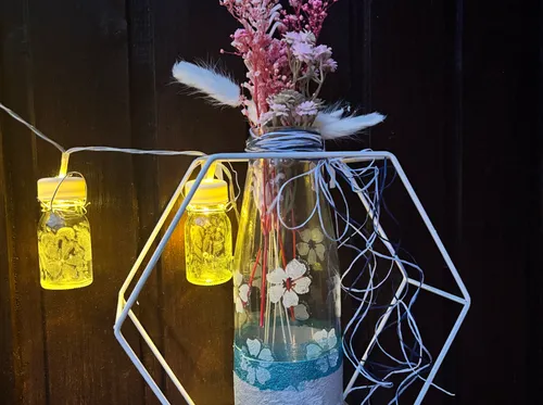 Bottle with flowers, hanging lights, dark background.