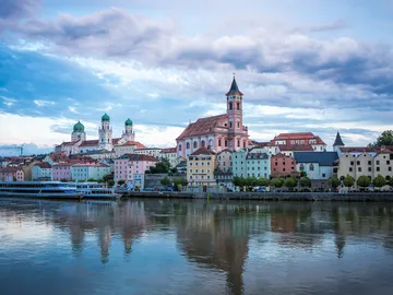 Colourful buildings are reflected in the quiet river under clouds.
