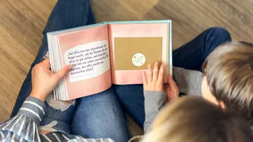Erwachsene lesen mit einem Kind ein Buch.