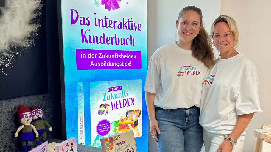 Two women standing beside a children's book sign.