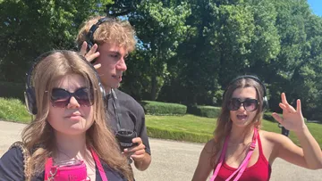 Three people with headphones outside on sunny day.