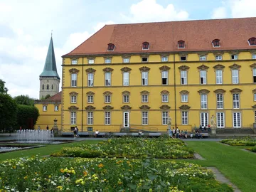 Yellow building stands in front of a well-kept garden with people.