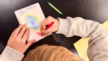 Child drawing with crayons on table.