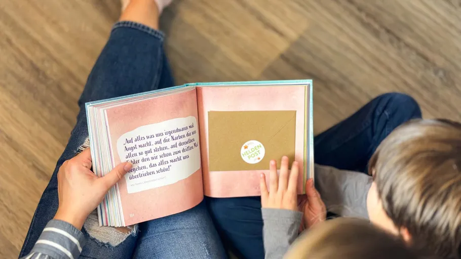 Book held by adult and child sitting on floor.