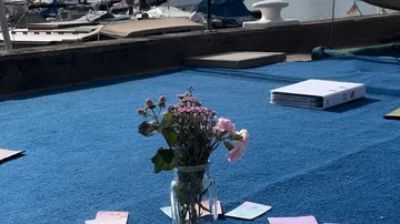 Flowers in vase on blue mat near boats.