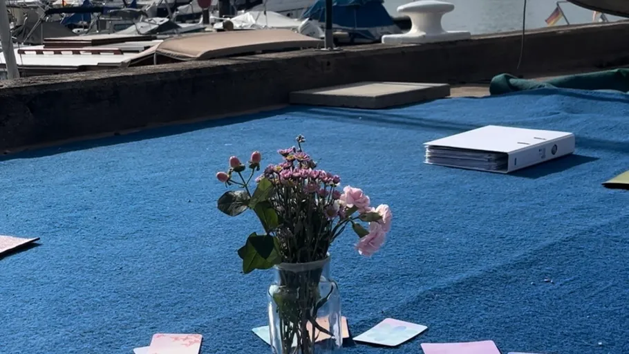 Flowers in vase on blue mat near boats.