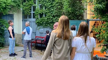 Personen stehen in einem bewachsenen Innenhof und diskutieren.