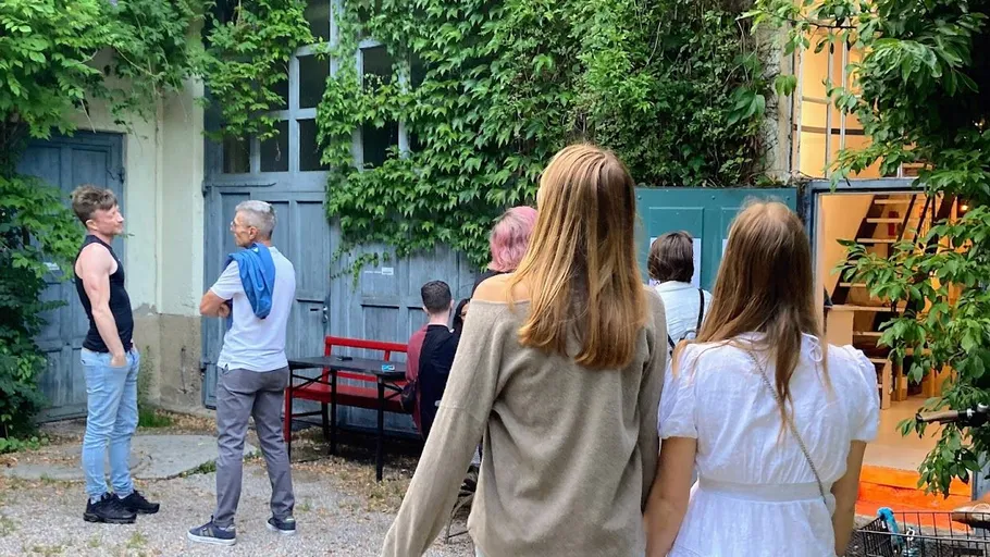 Personen stehen in einem bewachsenen Innenhof und diskutieren.