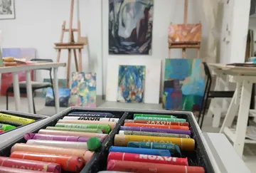 Pastels in art studio with colorful paintings.