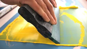 Hand using squeegee for screen printing.